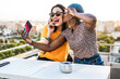 © ADDICTIVE STOCK - Happy lesbian couple taking selfie on balcony