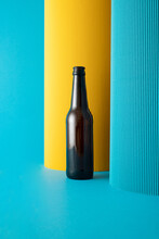 Brown Glass Beer Bottle And Two Paper Pillars - Yellow And Blue On Blue Background.