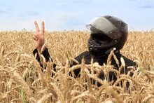 A Male Driver Full Motorcycle Equipped. Outdoor Wheat Field And Sky. Victory Sign Concept. Rider Equipment