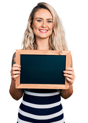 Poster - Young blonde woman holding blackboard smiling with a happy and cool smile on face. showing teeth.