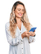 © Krakenimages.com - Young blonde woman using smartphone smiling with a happy and cool smile on face. showing teeth.
