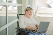 © Renata Hamuda - an elegant and smiling woman with disability sitting in a wheelchair enjoying computer work online