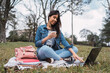 © ADDICTIVE STOCK - Young woman with drink and laptop in park