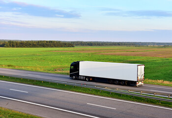 Wall Mural - Truck with semi-trailer driving on highway on sunset. Goods delivery by roads. Services and Transport logistics. Lorry Transport in motion. Long Self-driving lorries. Semi-trailer truck on freeway..