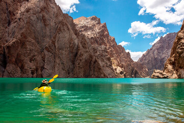 Wall Mural - Kayaking on a mountain lake. Two men are sailing on a yellow canoe along the lake along the rocks. The theme of water sports and summer holidays.