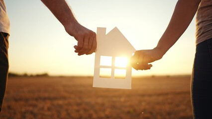 paper house happy family. friendly family hands holding paper house the glare of the sun shine through the window a beautiful sunset. mortgage business construction concept lifestyle. house dreams