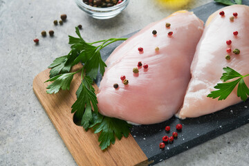 Wall Mural - Chicken breast. Two Chicken fillet with spices, olive oil and parsley on black stone cutting board on grey stone table background. Top view with copy space. Food meat cooking background.