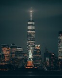 Fototapeta Kawa jest smaczna - Vertical shot of the Statue of Liberty and skyscrapers at night in New York, United States