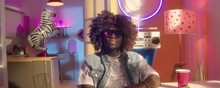 Zoom In Portrait Shot Of African American Guy In Sleeveless Denim Jacket And Trendy Sunglasses Posing On Camera In Bright Colored Room With Neon Decorations
