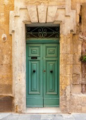 Poster - Vertical shot of a vintage green front door of a yellow brick building in Valetta, Malta