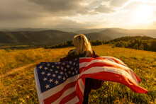 Woman Holding USA Flag On Top Of Mountain And Enjoys The View Of The Autumn Rocks Hills. Celebrating Independence Day Of America.