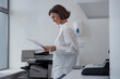 Smiling woman worker scanning a document on photocopy machine In modern office. Blurred background