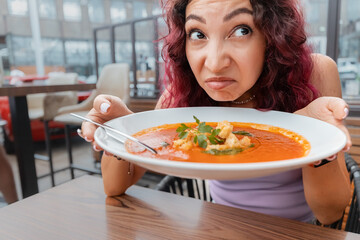 A woman dissatisfied customer of the restaurant sniffs the disgusting smell of a bowl of soup with spoiled ingredients and is going to complain to the chef