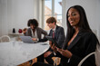 © Media Lens King - Portrait of an African businesswoman in the office dressed elegantly holding a tablet with her colleagues in the background working.