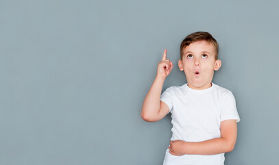 Wall Mural - European handsome little boy is surprised, inspired, i have an idea, raise your index finger up, copy space, isolated on gray background. schoolboy