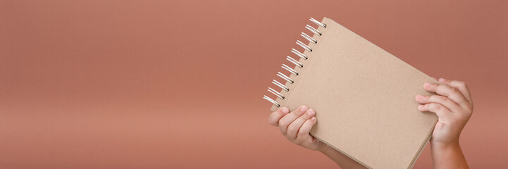 Wall Mural - Notepad in hand. Blank notepad in the hands of a child on a red background. Hands hold a book without text. The girl is holding a book with an empty cover.