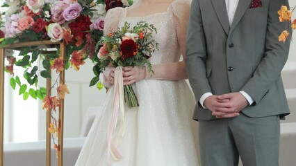 Wall Mural - Bride in white dress and groom in grey suit on wedding ceremony. beautiful wedding bouquet in red, pink, white pastel colours and greenery in hands of bride at wedding celebration