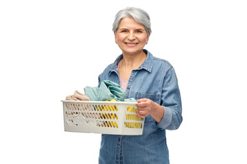 Poster - cleaning, wash and old people concept - portrait of smiling senior woman in denim shirt with towels in laundry basket over white background