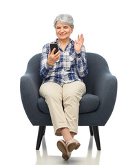 Canvas Print - comfort, furniture and old people concept - smiling senior woman with smartphone having video call and sitting in modern armchair over white background