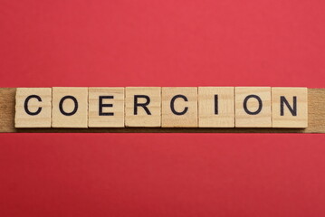 text the word coercion from gray wooden small letters with black font on an red table
