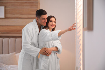 Canvas Print - Happy couple wearing bathrobes near window in bedroom