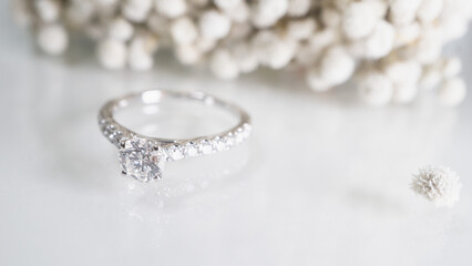 Close up of diamond ring with white flower, sunlight and shadow background. Love, valentine, relationship and wedding concept. Soft and selective focus.