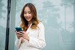© sorapop - Asian businesswoman working with mobile phone standing against street front building near office, Portrait successful business woman smiling holding smartphone use application chat online in morning