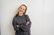 © contrastwerkstatt - young redhead woman stands laughing with folded arms in front of white wall