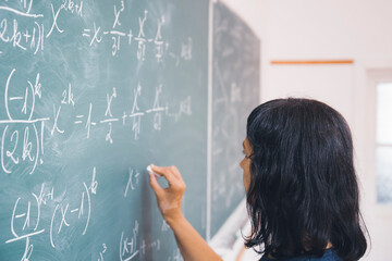 Female student or teacher in the classroom writing on chalkboard mathematical equations