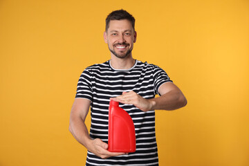 Wall Mural - Man holding red container of motor oil on orange background