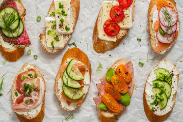 Variety of small sandwiches with cream cheese, vegetables and salami.