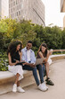 © Look! - Happy young interracial students use laptop and tablet preparing for their lessons outdoors. Brunette guy and girls wear casual clothes in summer. Technology concept