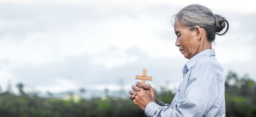 Wall Mural - Old woman praying with holding cross in hands. Christian Religion concept background. Copy space for your individual text.