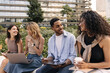 © Look! - Diverse young students are developing spreadsheet based on lectures laptop and tablet sitting outdoors. Guy and girls communicate on educational topics. Technology concept