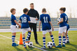 © matimix - Football coach coaching children. Young coach teaching kids on football field. Trainer explains to schoolboys training rules. Soccer football training session for children. Football tactic education.