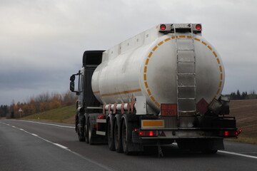 Wall Mural - Old semi truck fuel tanker with 33-1203 dangerous class sign move on suburban highway road at autumn evening in perspective, back view, gasoline fuel ADR cargo transportation logistics in Europe