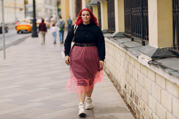 Wall Mural - Young plus size woman. Young red pink haired body positive girl walking at city street outdoors