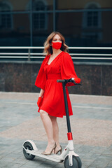 Wall Mural - Young woman with electric scooter in red dress and gloves with medical face mask at the city.