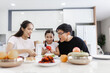 © nikomsolftwaer - Asian family having meals together and showing thumbs up at home happily, Happy young parents are having fun with their little daughter during lunch at the dining table.