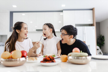 Asian family having meals together and showing thumbs up at home happily, Happy young parents are having fun with their little daughter during lunch at the dining table.