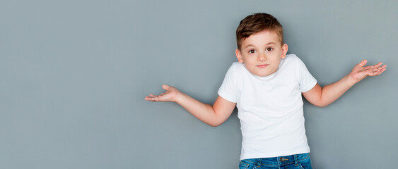 Little cute boy kid wearing casual white tshirt clueless and confused expression with arms and hands raised. doubt concept.