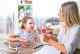 Fototapeta Łazienka - Doctor and small patient train articulation, work on problems and obstacles child with dyslexia. little girl together with speech therapist is sitting at desk indoors, playing game, studying sounds