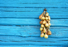 Garland Made Of Onions Is Hanged On A Wooden Blue Wall To Dry Up For Conservation. Rustic Log Background. Copy Space,