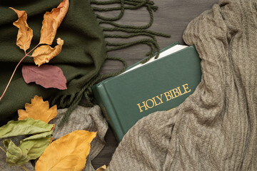 Wall Mural - Closed Christian bible with green blanket and autumn leaves on a dark wood background