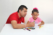© Arlette - Latino dad and daughter, teacher and student draw in a notebook with colors in this back to school to improve skills with Autism Spectrum Disorder (ASD)