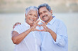 © Alexis Scholtz/peopleimages.com - A happy senior couple with a heart sign with their fingers and enjoying fresh nature air on vacation at beach while bonding. Portrait of retired couple hugging at beach with smile and love together