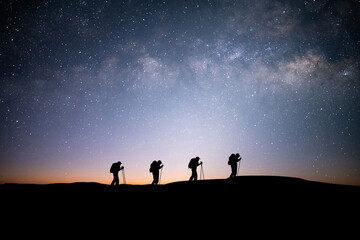 Wall Mural - Silhouette of four young traveler and backpacker hiking to the top of the mountain with beautiful view star, milky way over the sky. He enjoyed traveling and was successful when he reached the summit.