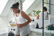 © gpointstudio - Young African-American woman standing in the bathroom and feeling pain in the stomach