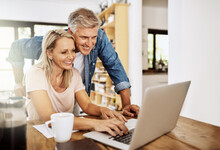 Happy, Smiling And Mature Couple Using A Laptop Together At Home. Charming Husband Assisting Wife With Online Work On The Internet. Cheerful Middle Aged Partners Working As A Team On Social Media.