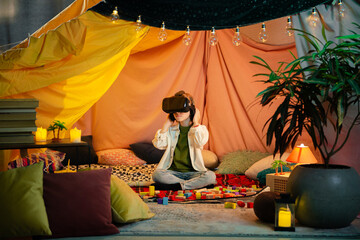 The boy are hanging out in a children s blanket tent indoors while playing with a vr headset and enjoying their time laughing together